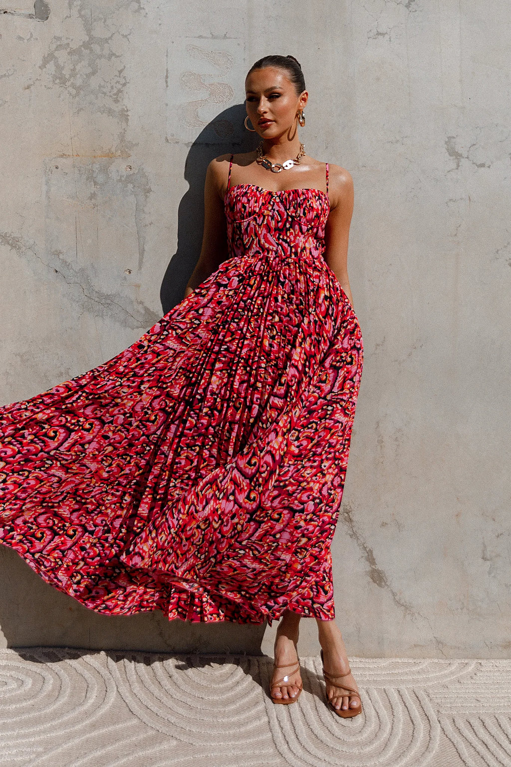 Side view of a pink pink multi pleated maxi dress, worn by a model against a plain studio backdrop