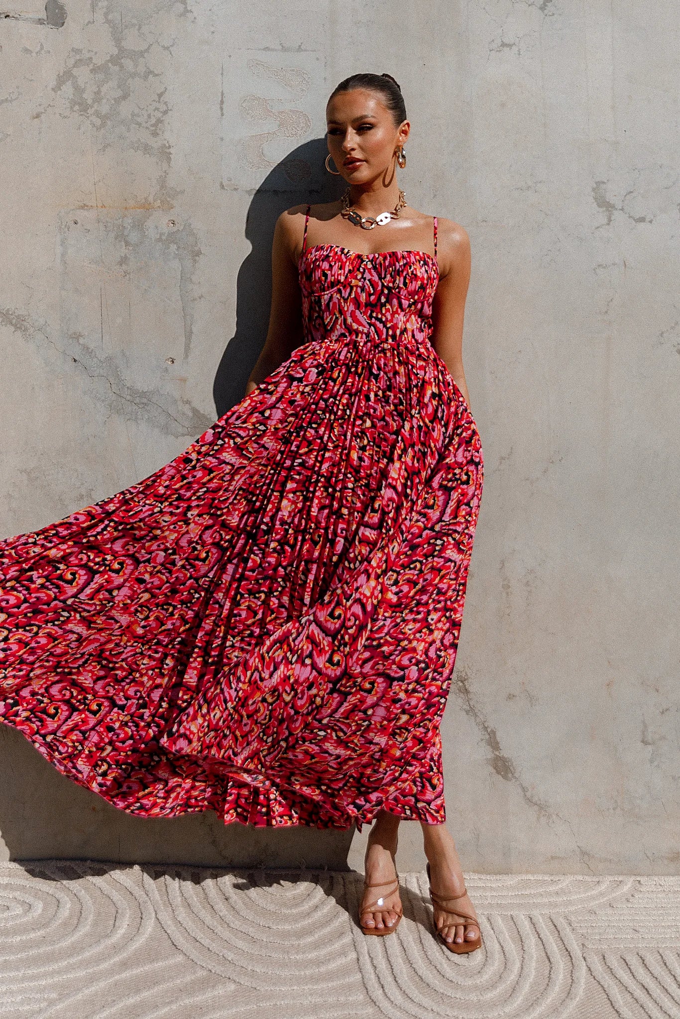Side view of a pink pink multi pleated maxi dress, worn by a model against a plain studio backdrop