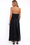 Front view of a black strapless black maxi dress, bow back, worn by a model against a plain studio backdrop