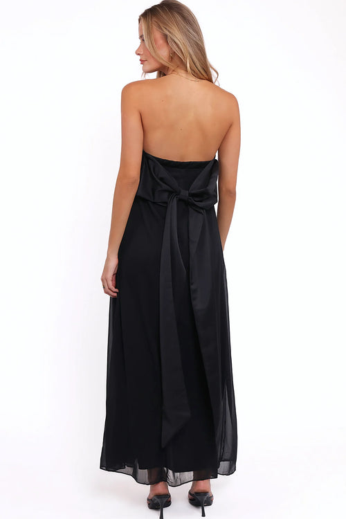 Front view of a black strapless black maxi dress, bow back, worn by a model against a plain studio backdrop