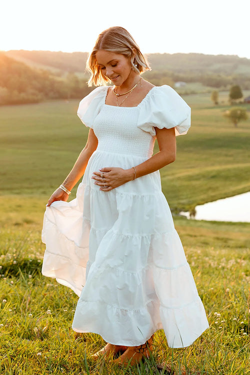 Back view of a white white smocked puff sleeve midi dress, worn by a model against a plain studio backdrop