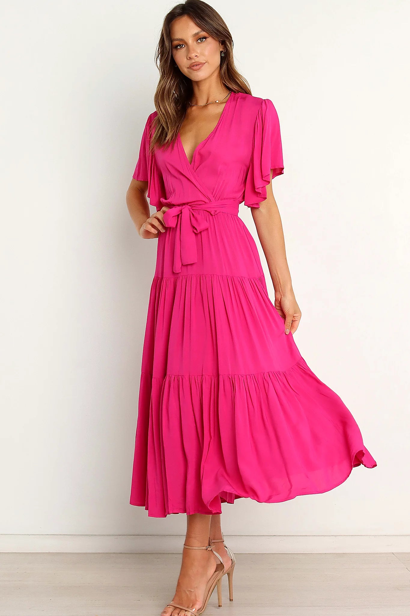 Side view of a pink pink ruffle sleeve tiered midi dress, worn by a model against a plain studio backdrop