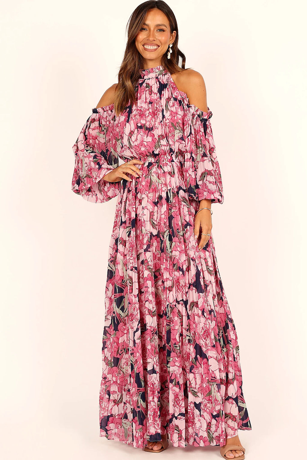 Close-up detail of a pink pink floral pleated maxi dress, worn by a model against a plain studio backdrop