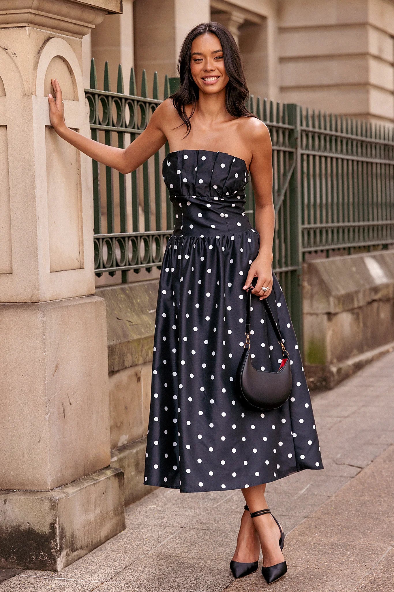 Back view of a line polka dot strapless midi dress, a, worn by a model against a plain studio backdrop