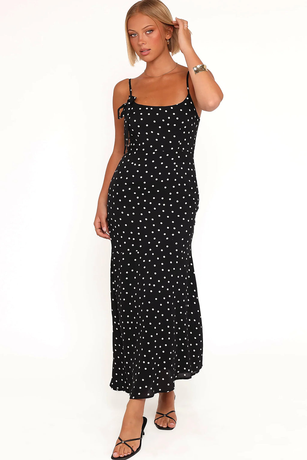Back view of a black polka dot midi dress, worn by a model against a plain studio backdrop