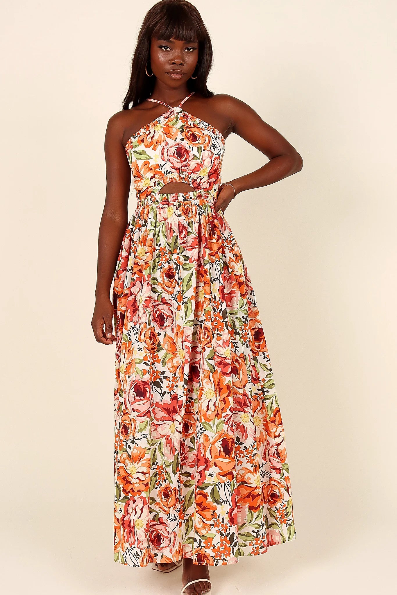 Close-up detail of a orange floral halterneck maxi dress, worn by a model against a plain studio backdrop