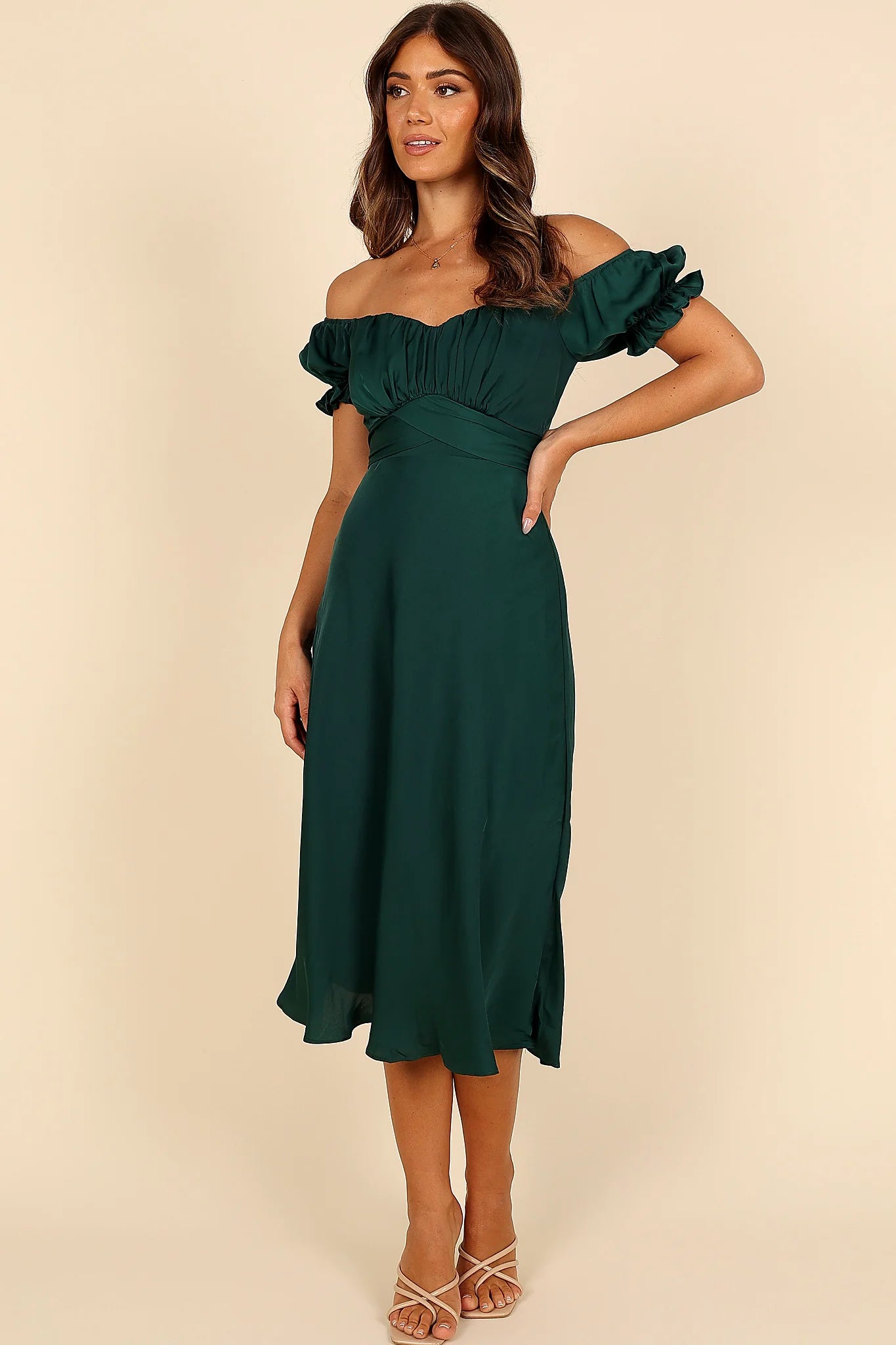 Close-up detail of a green emerald off shoulder frill midi dress, worn by a model against a plain studio backdrop