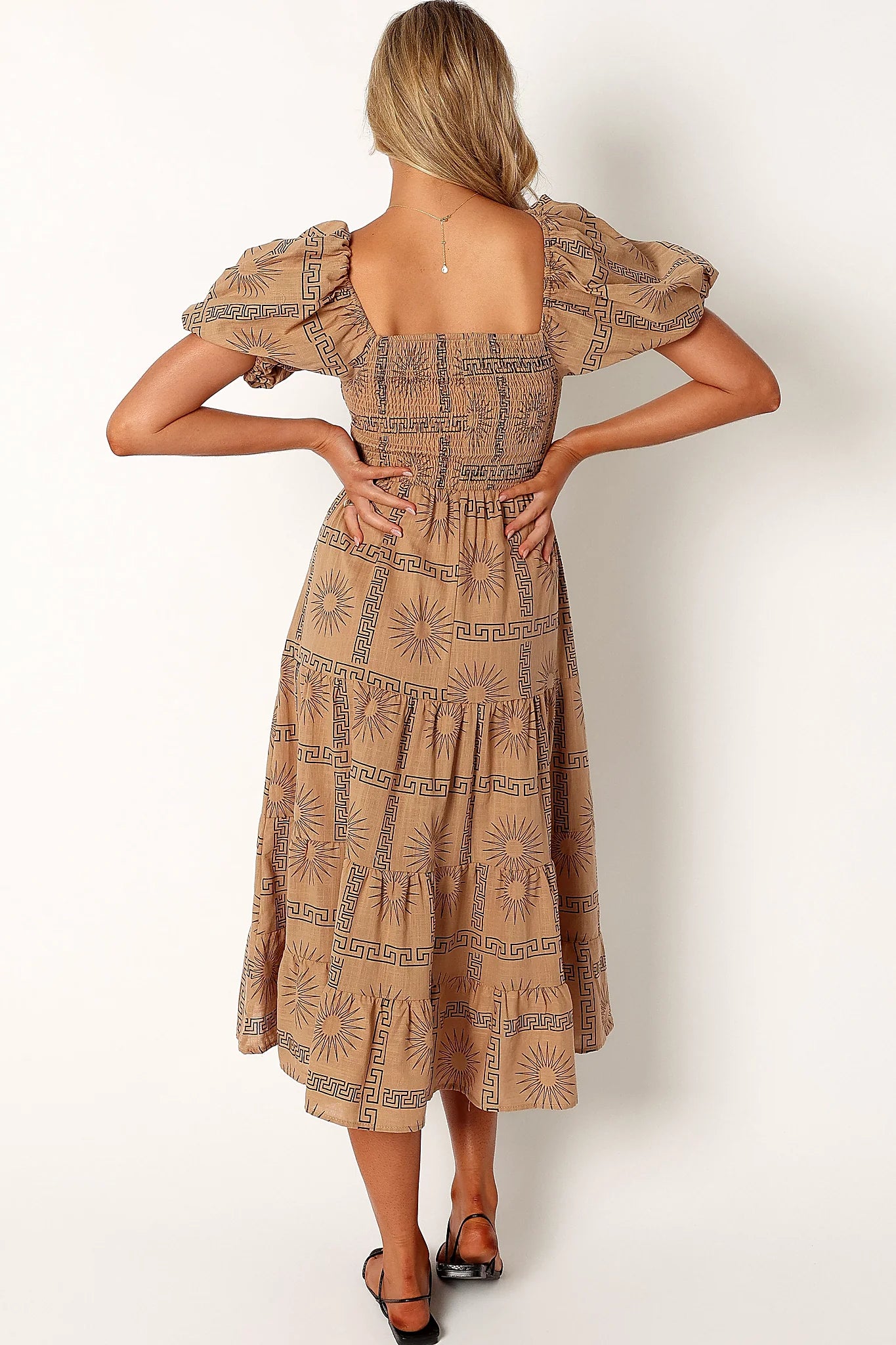 Close-up detail of a black tan & black sun print midi dress, worn by a model against a plain studio backdrop