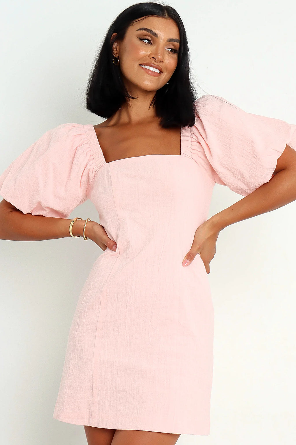 Back view of a pink baby pink puff sleeve mini dress, worn by a model against a plain studio backdrop